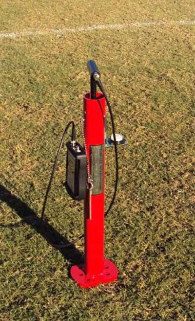 Red Clegg hammer testing surface hardness on a sports field beside a painted line