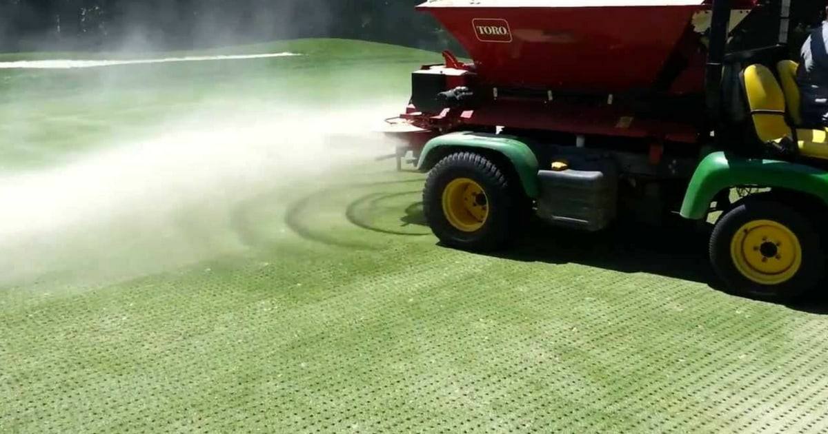 Topdresser on a utility vehicle spreading sand over freshly cored turf
