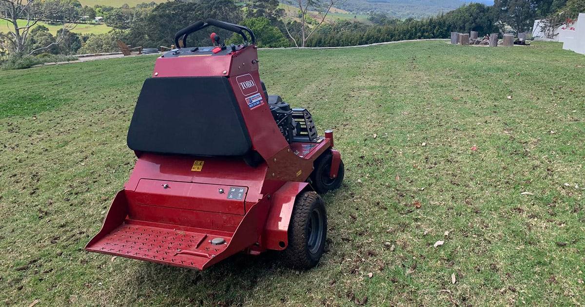 Toro stand-on core aerator on a sloping acreage lawn, with soil cores across the grass