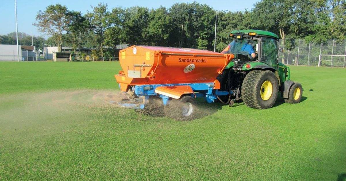 Tractor-towed spreader top dressing a football field with sand