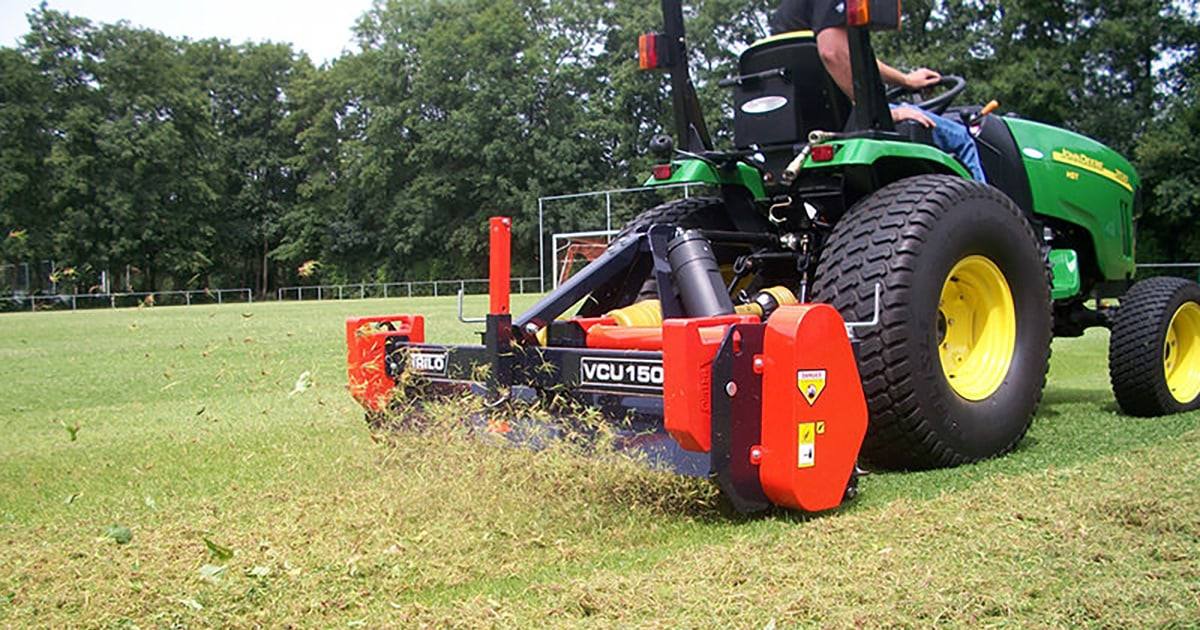 Tractor-mounted scarifier cutting thatch out of a sports field